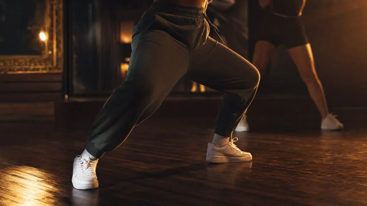 Tänzerin in tiefer Reggaeton-Haltung, Sneaker auf dem Parkett im Gegenlicht